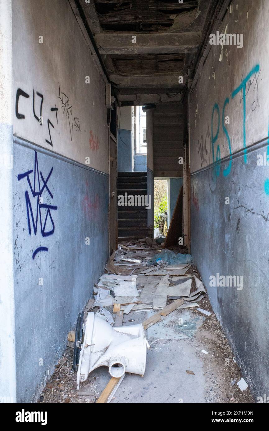 Abandoned and derelict corridor and stairwell in a tenement building in Clune Park, Port Glasgow. Graffiti on wall and broken toilet. Stock Photo