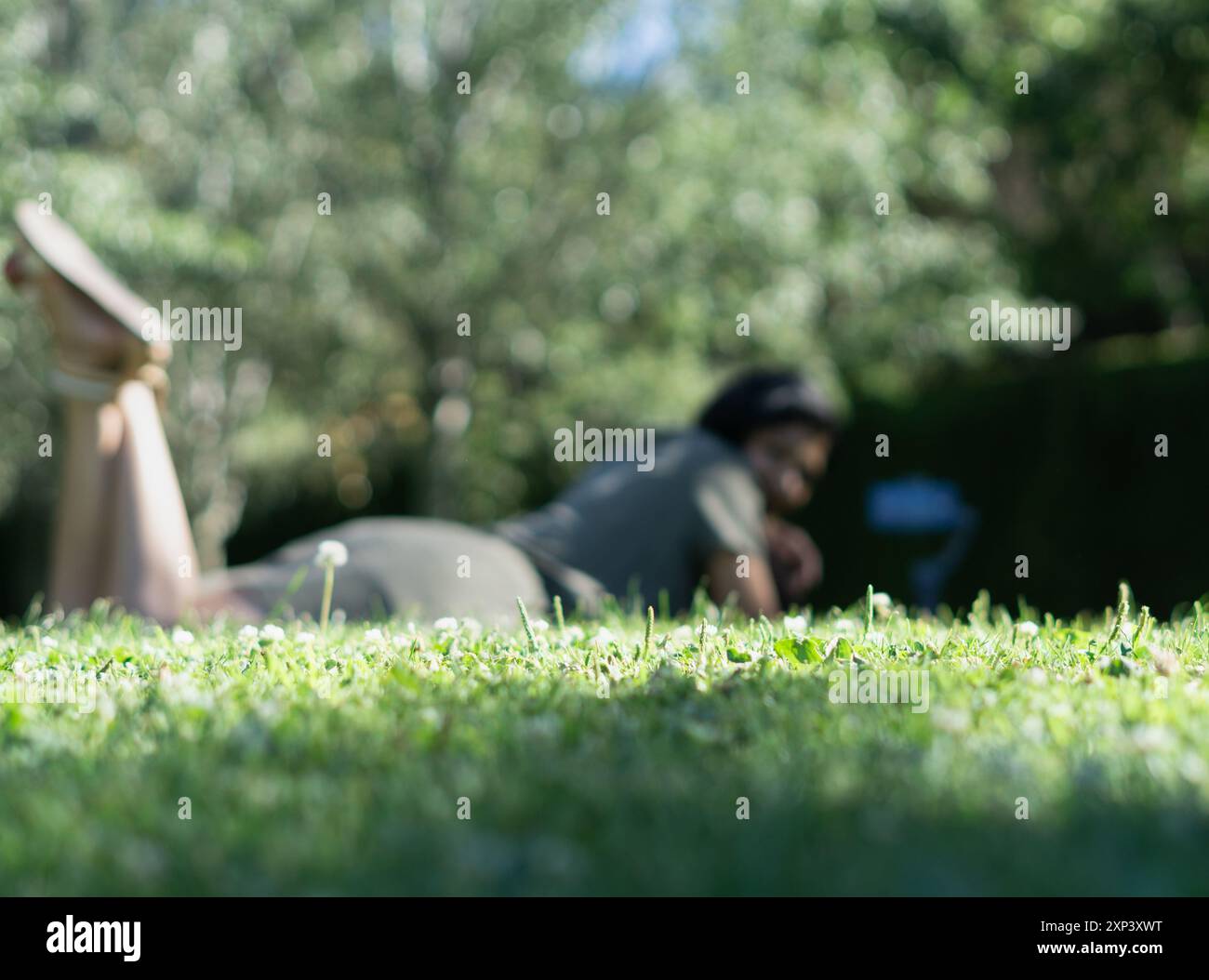 A woman is laying on the grass in a park. The grass is green and the ...