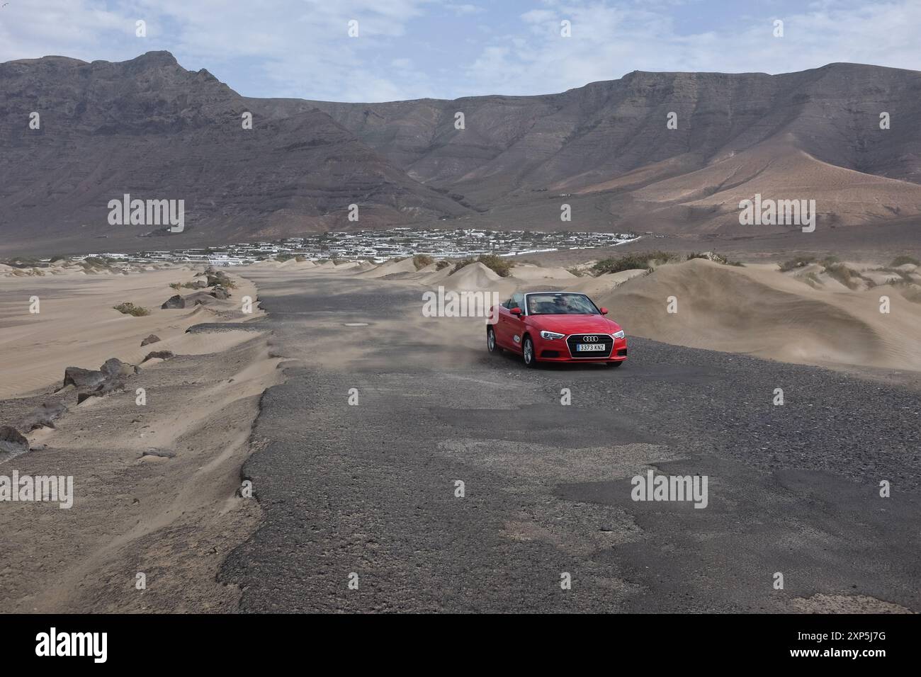 The road going from the bungalows Los Noruegos to the Caleta de Famara, with a solitary red Audi convertible. Famara, Lanzarote. Stock Photo