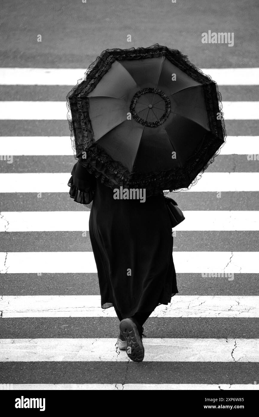 Woman in black with a black umbrella crossing a pedestrian crossing ...