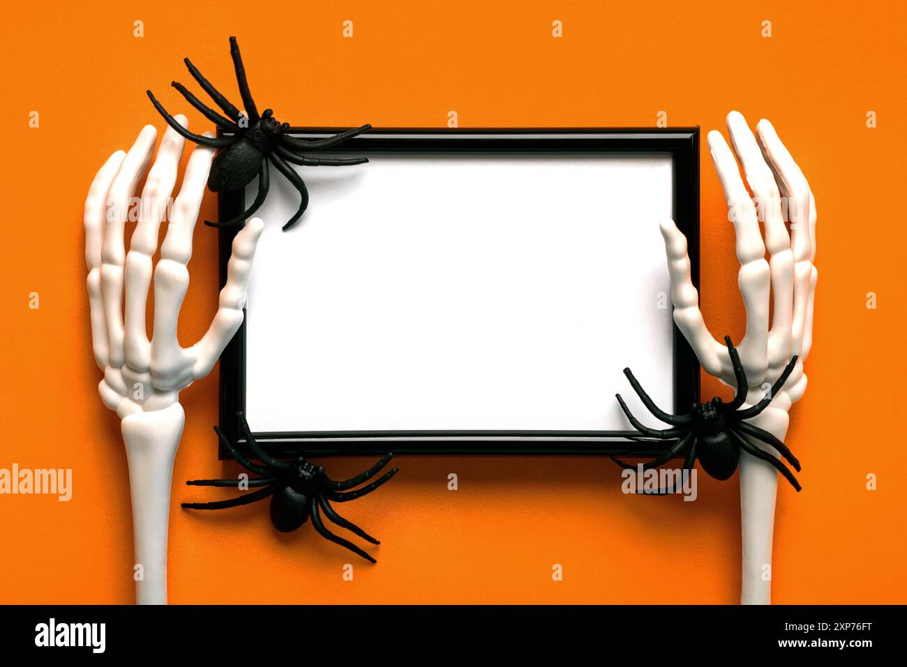 Top view of black frame with spiders,skeleton hand bones with space for text over orange background. Halloween concept background Stock Photo