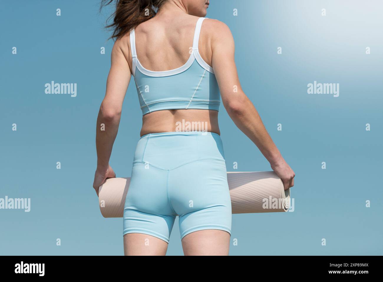 Fit, sporty woman carrying an exercise mat, outdoors, rear view. Stock Photo