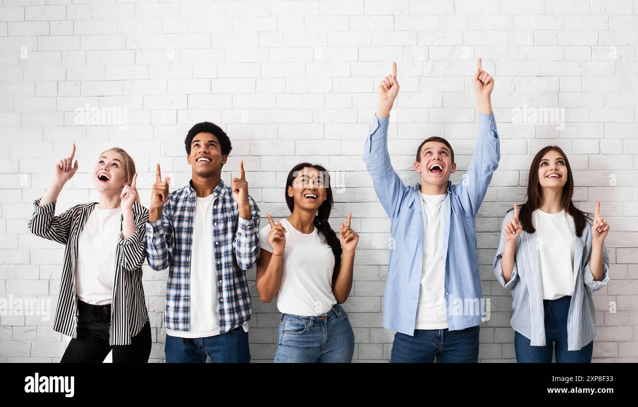 Teens pointing up on free space over white brick wall Stock Photo