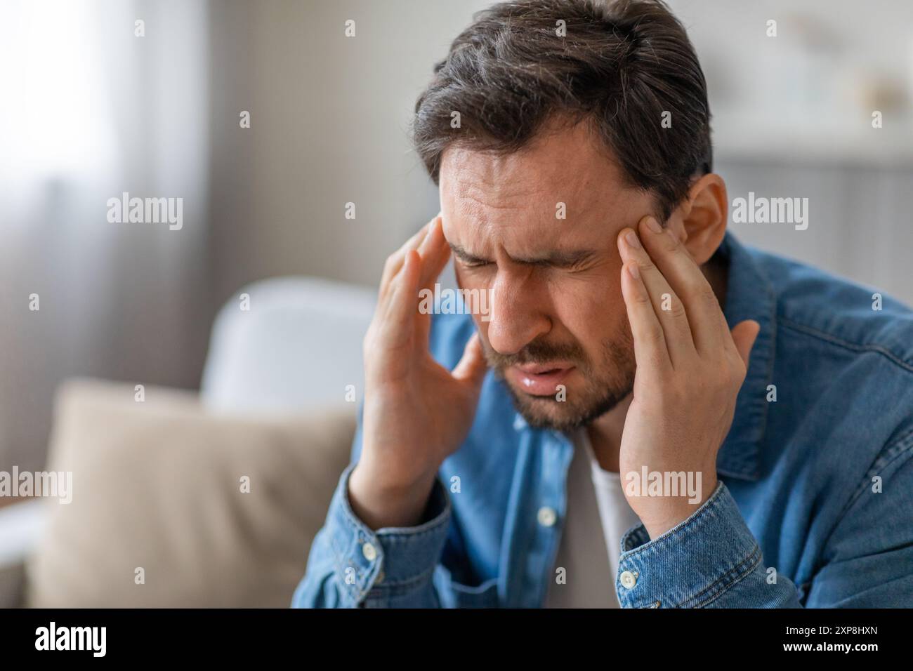 Man Holding His Head in Pain While Sitting on Couch Stock Photo - Alamy