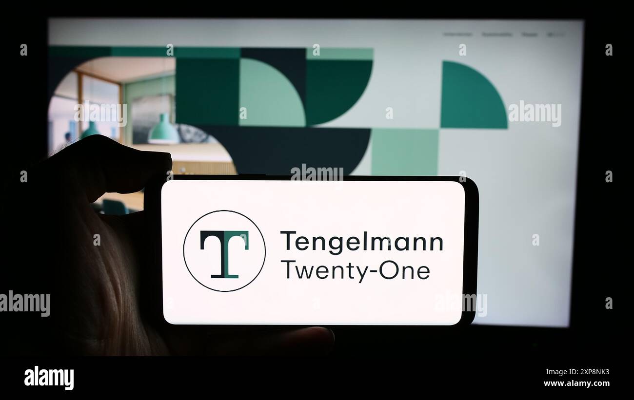 Person holding cellphone with logo of German holding company Tengelmann Twenty-One KG in front of business webpage. Focus on phone display. Stock Photo