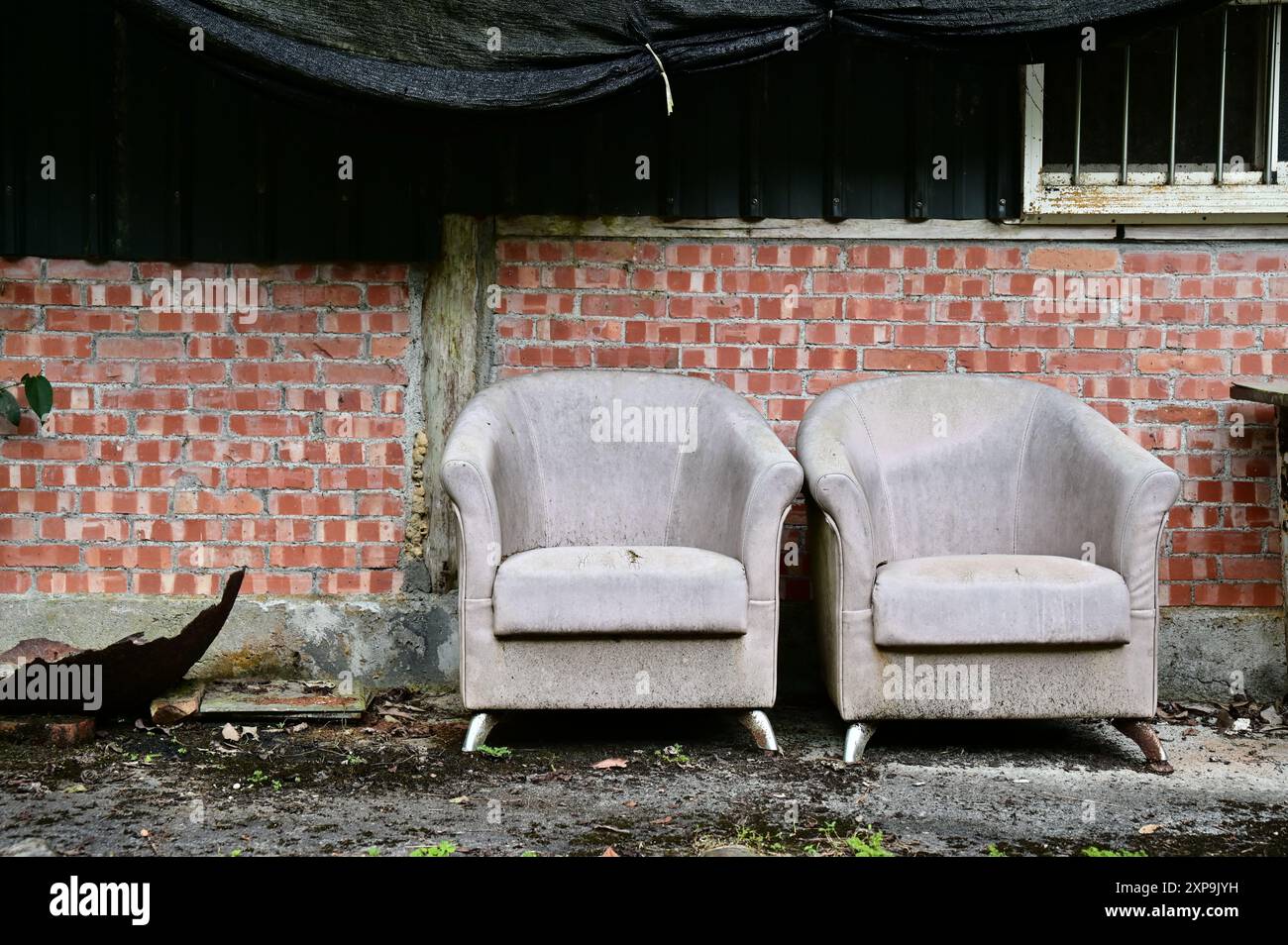 Capture the charm of a weathered red brick house with old sofas outside, evoking nostalgia and tranquility on a cloudy afternoon. Stock Photo