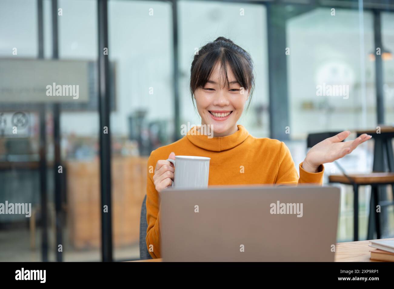 A beautiful, cheerful Asian woman is working remotely from a coffee ...