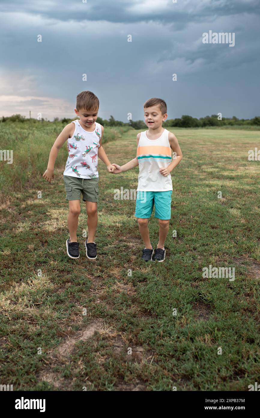 Two boys playing and jumping in grassy field under overcast sky
