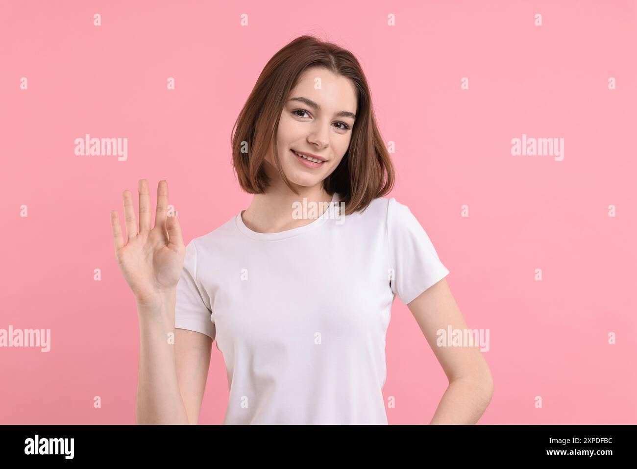 Happy teenage girl waving on pink background Stock Photo