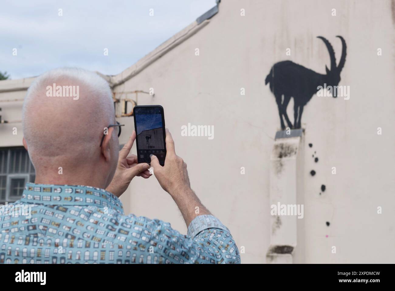 London, UK. 05 Aug 2024. People take photos of Street Artist Banksy's latest artwork depicting a mountain goat perched on a building's column with rocks falling off at Kew Bridge. Credit: Justin Ng/Alamy Live News. Stock Photo