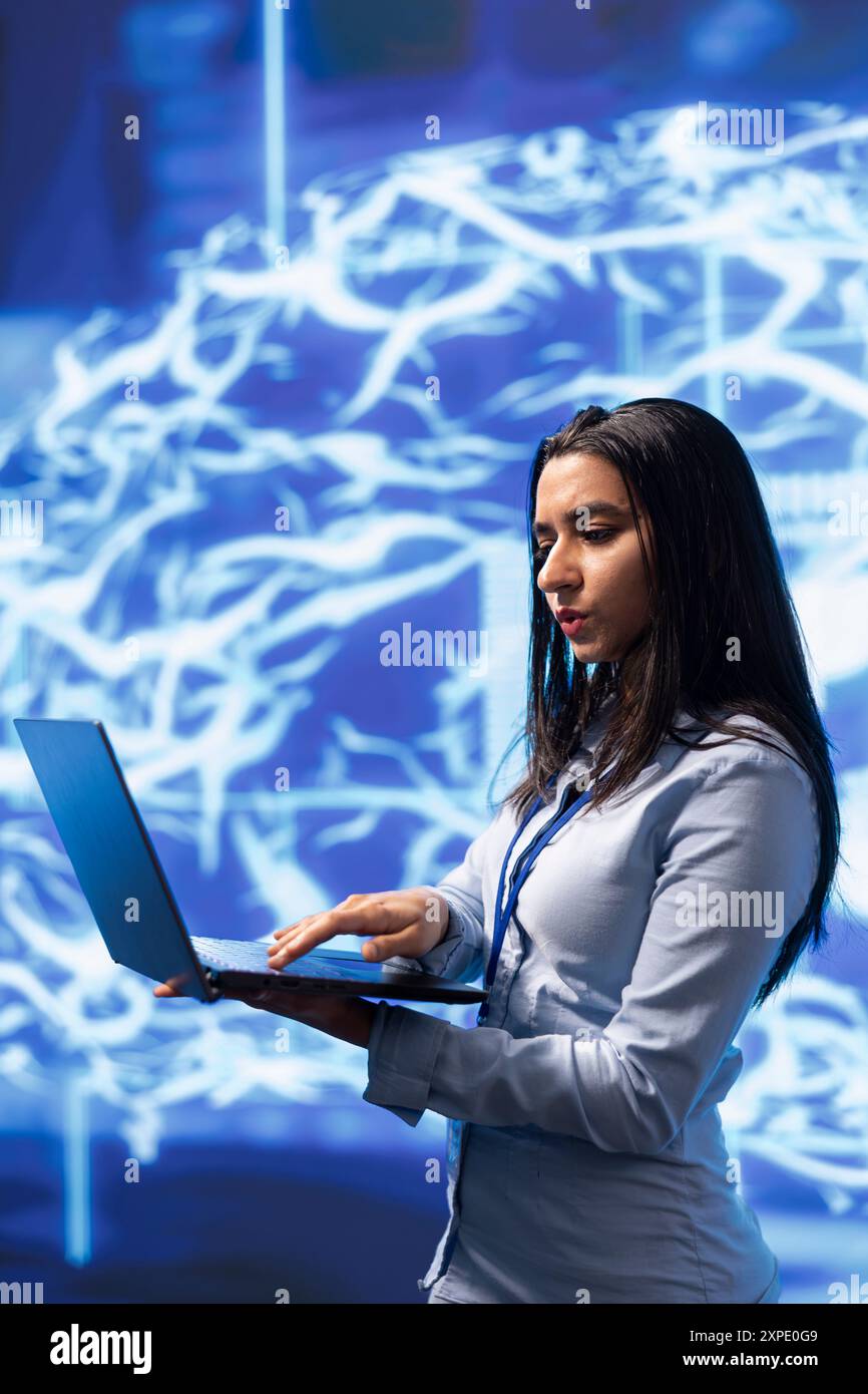 Software engineer solving tasks on laptop, running artificial intelligence programming scripts. Woman in modern lab using notebook to write lines of code for AI applications development Stock Photo