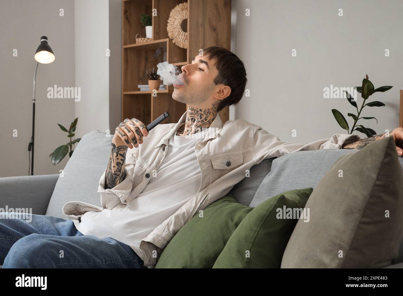 Young man smoking disposable electronic cigarette at home Stock Photo