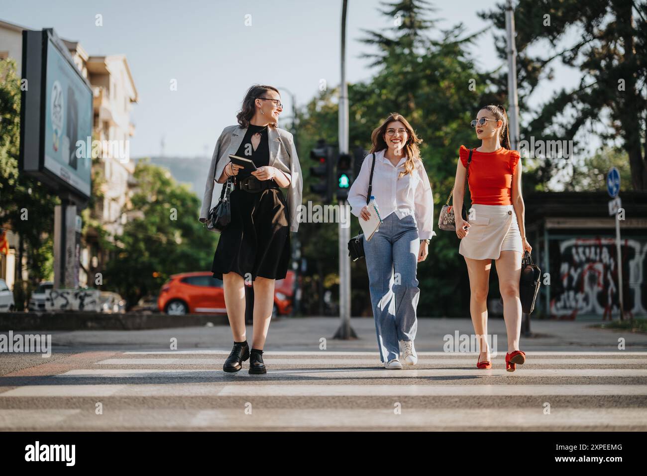 Three stylish businesswomen walking across a city street in the daytime ...