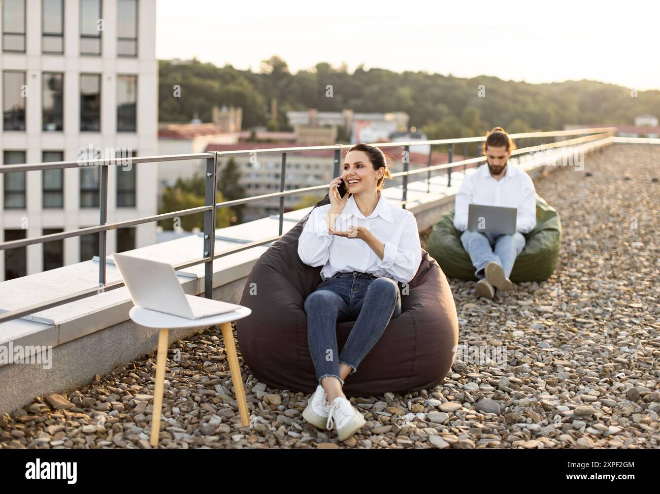 Young professionals working remotely on rooftop with laptops Stock Photo