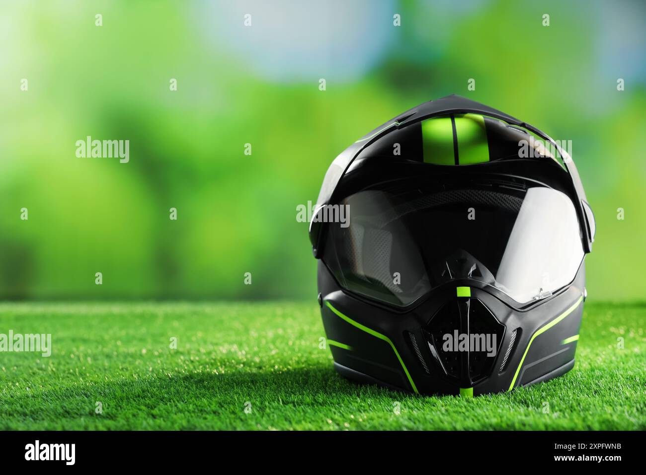 Modern motorcycle helmet with visor on green grass, space for text ...