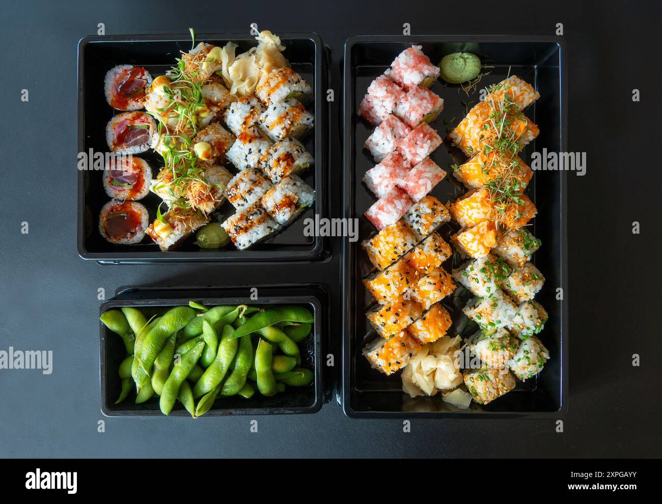 Delicious sushi rolls side by side and Sweet edamame peas in  black trays. Top view on blue and black background. Stock Photo