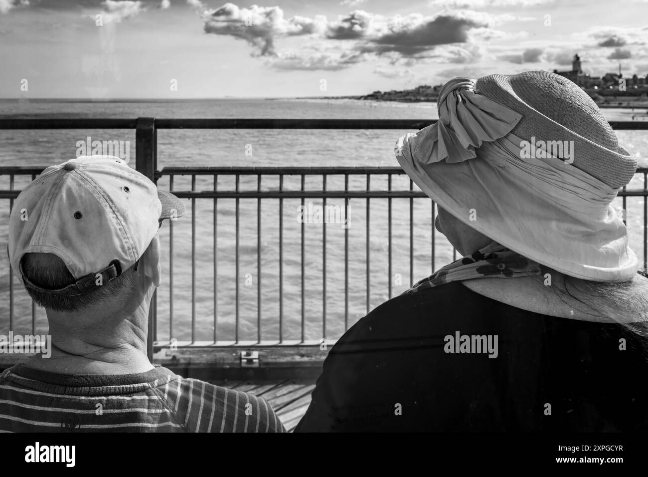 Rear view of an elderly couple sitting together looking out to sea on Southwold Pier in Summer 2024. Abstract. Black and White image. Stock Photo