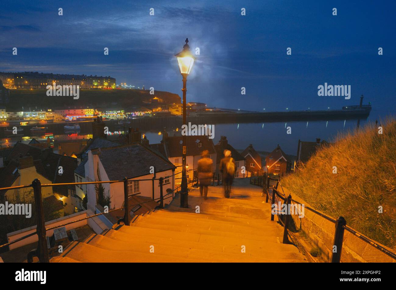 People walking down the famous 199 steps at night to Whitby old town with view of the river esk, harbour and pier, North Yorkshire coast, England, UK Stock Photo