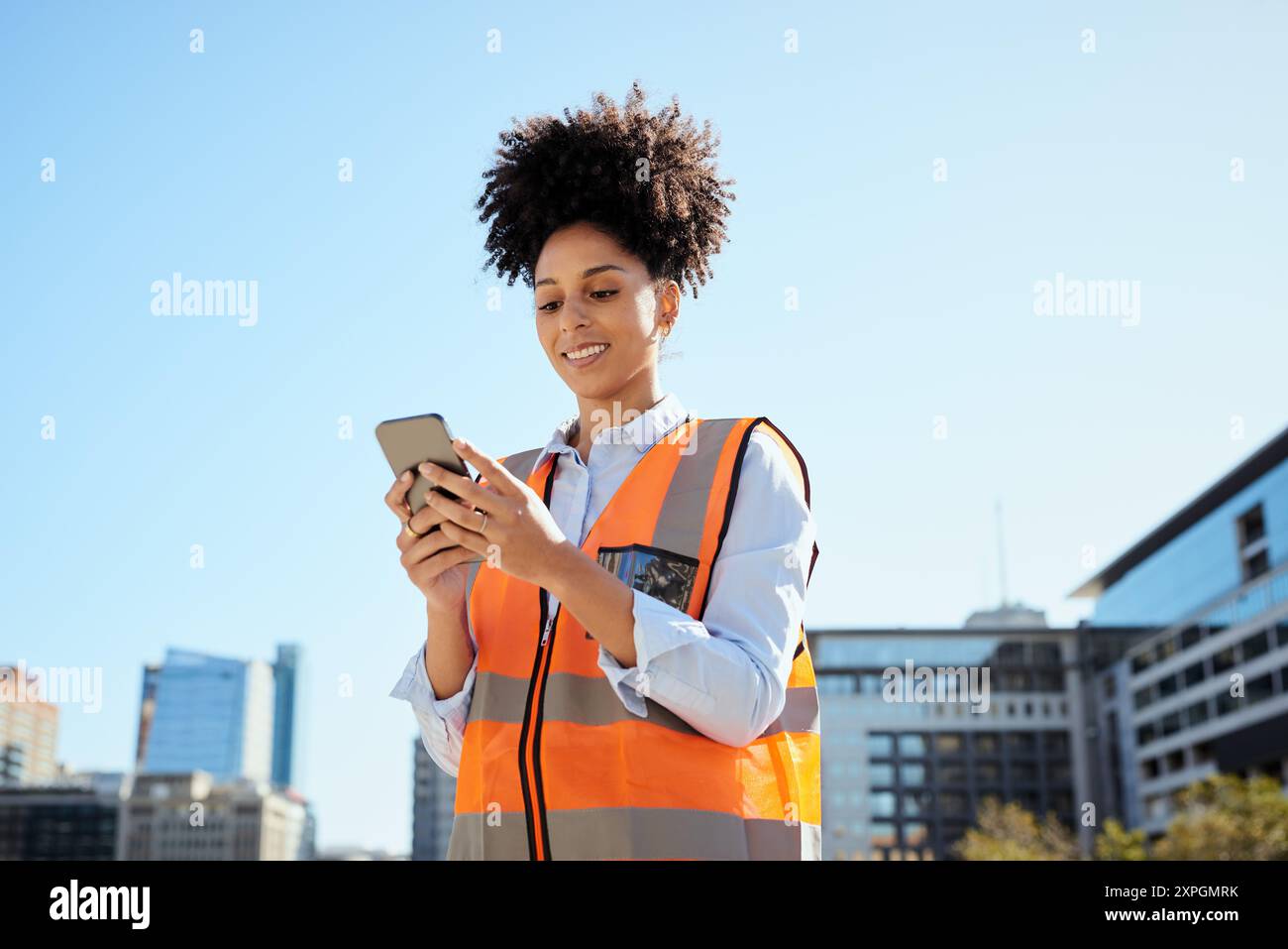 Confident Female Construction Worker Using Smartphone at Modern Urban Construction Site Stock Photo