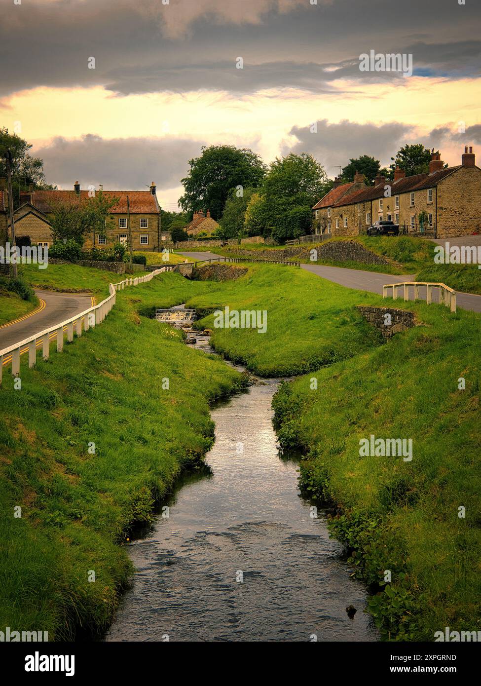 Looking along the beck in Hutton le Hole, a charming, beautiful village in North Yorkshire with golden, post storm light bathing the water Stock Photo