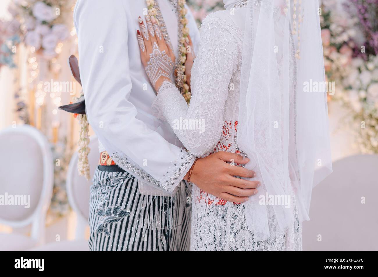 The bride and groom dressed in beautiful pure white traditional Javanese kebaya are posing in a romantic embrace Stock Photo