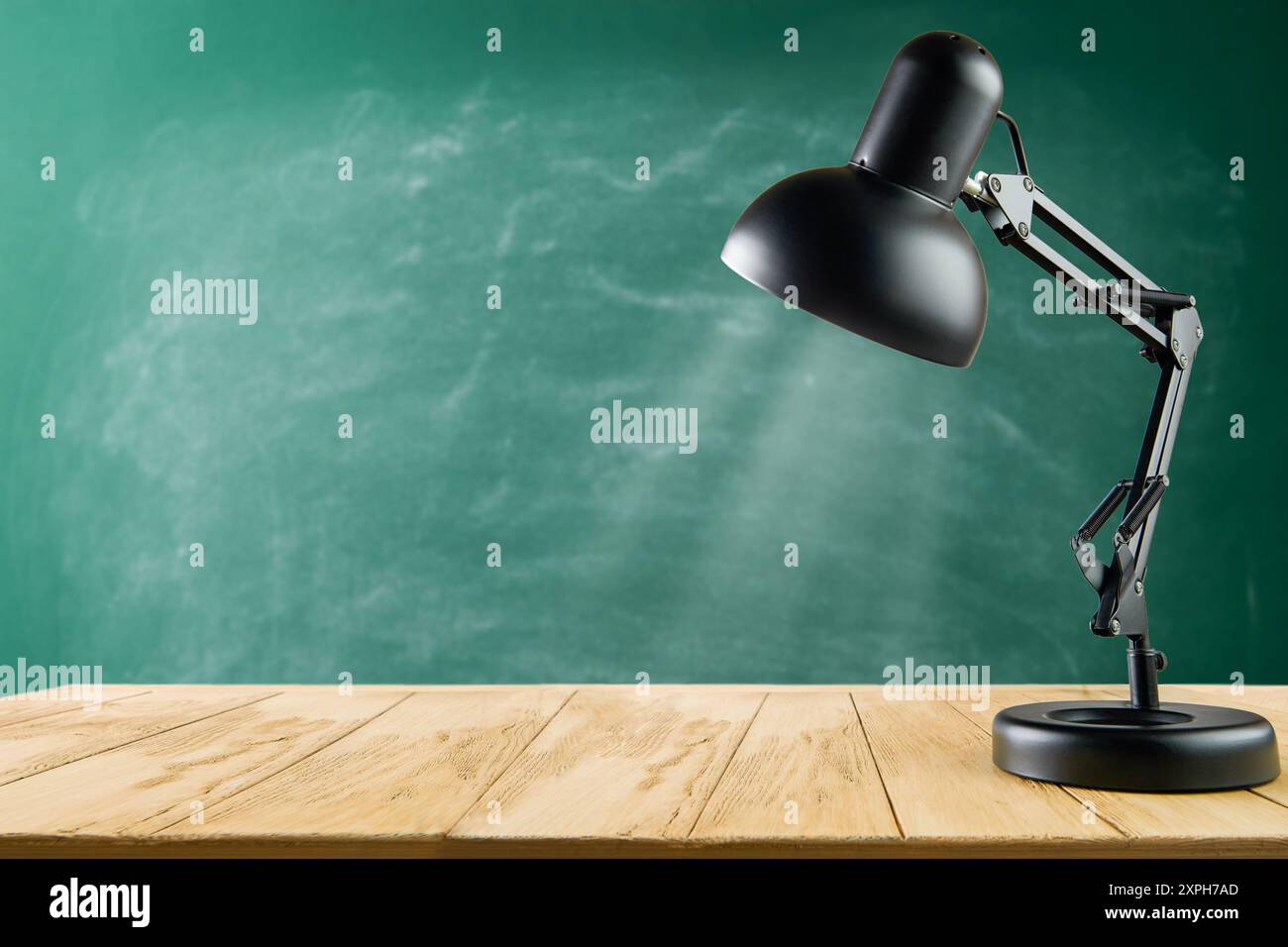 Black desk lamp on wooden table against green school chalkboard background. Back to school concept with copy space. Empty background. Stock Photo