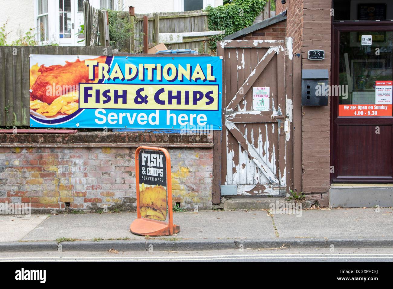 By a fish and chip shop in Framlingham a banner advertising the traditional takeaway and a door with peeling brown paint and an anti-litter sign. Stock Photo