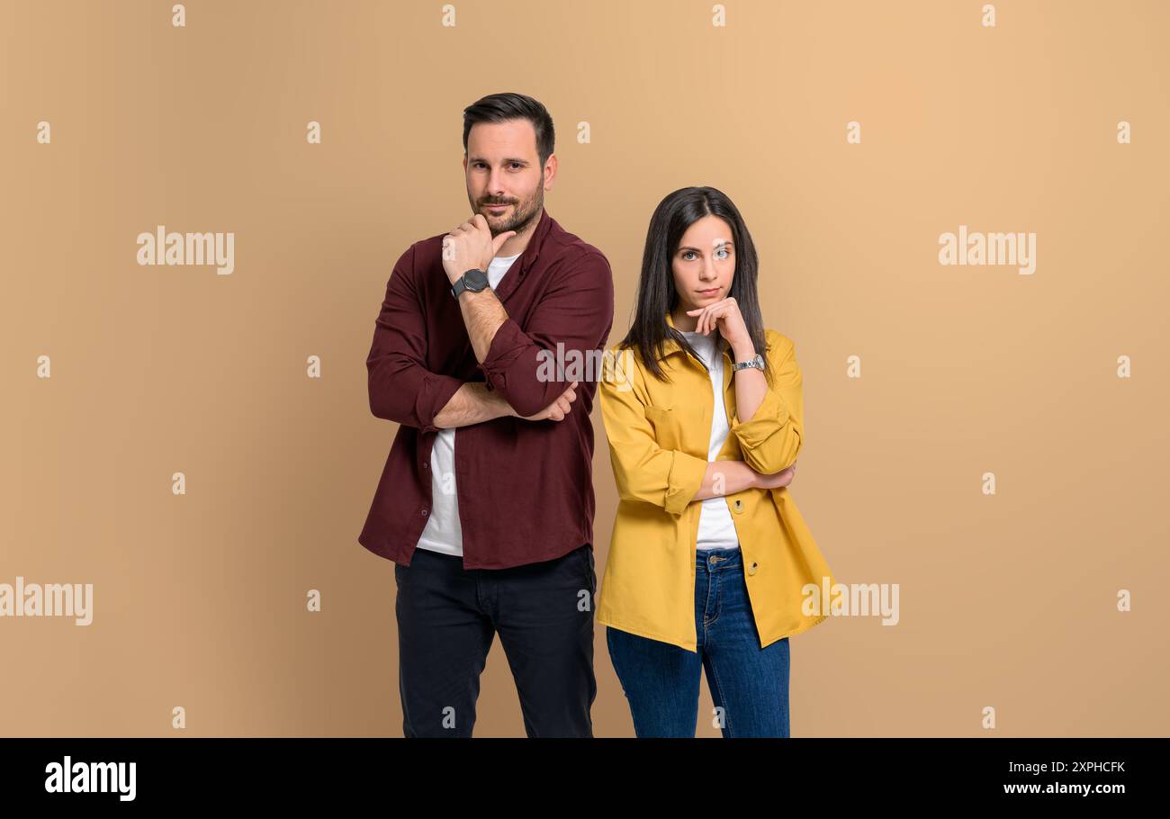 Charming young man and woman dressed in casuals touching chins and standing confidently on isolated beige background. Portrait of couple posing with a Stock Photo