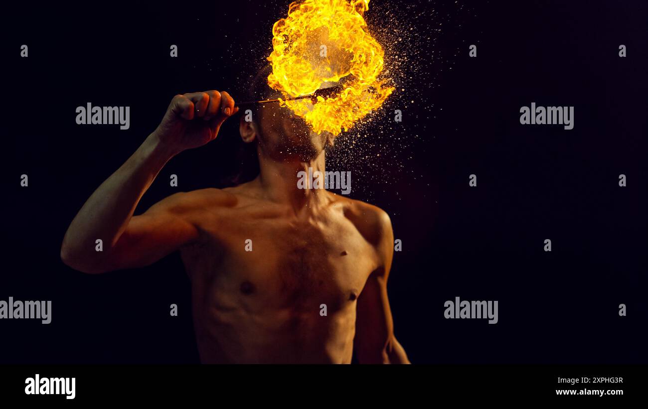 Male Fire Performer Skillfully Breathes Blazing Fireball, Creating Mesmerizing Spectacle of Flames and Sparks Against Dark Background. Cinematic Artistry of Fire Breathing Performance Stock Photo