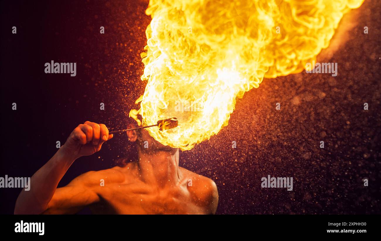 Male Fire Performer Dramatically Exhales Massive Fireball, Creating Stunning Visual of Flames and Sparks Against Dark Backdrop, Highlighting the Intensity and Skill of Fire Breathing Artistry. Stock Photo