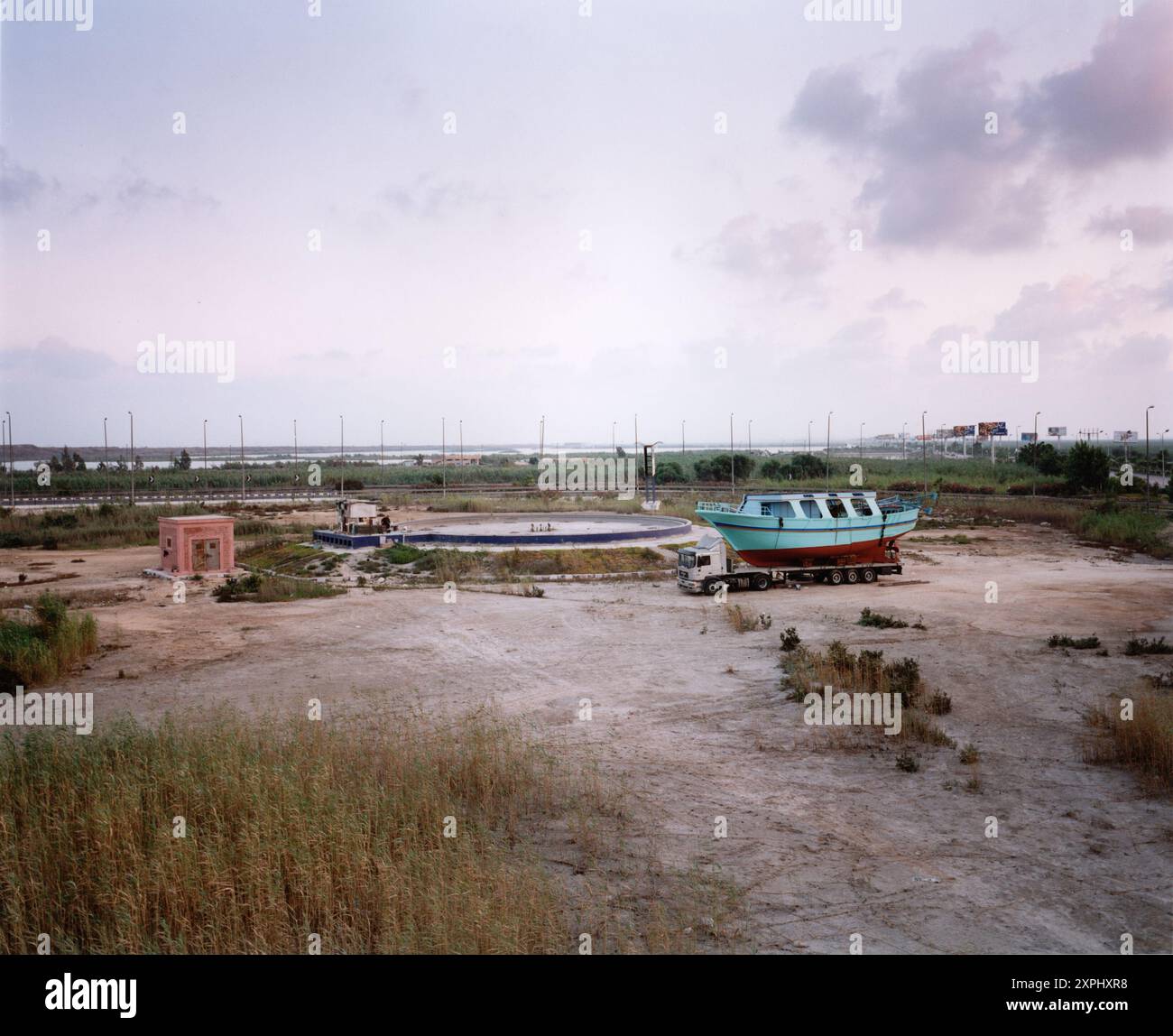 An image capturing a truck carrying a boat at a deserted area near Mariott Lake in Alexandria, Egypt, in 2006. The scene depicts a serene yet industrial environment. Stock Photo