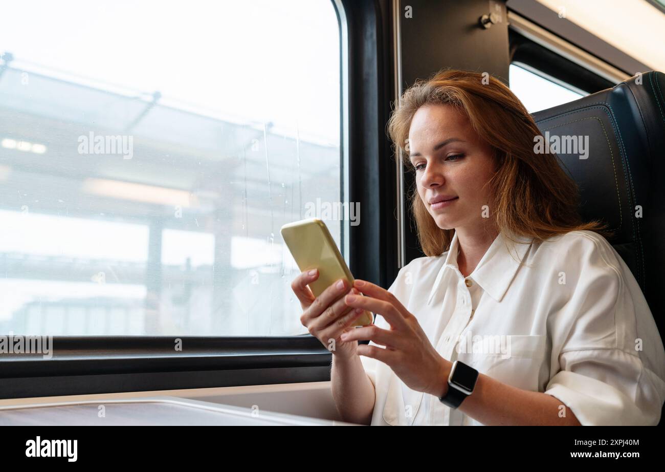 Modern tech-savvy businesswoman messaging online with her smartphone while traveling for work by train. Work on the go. Stock Photo