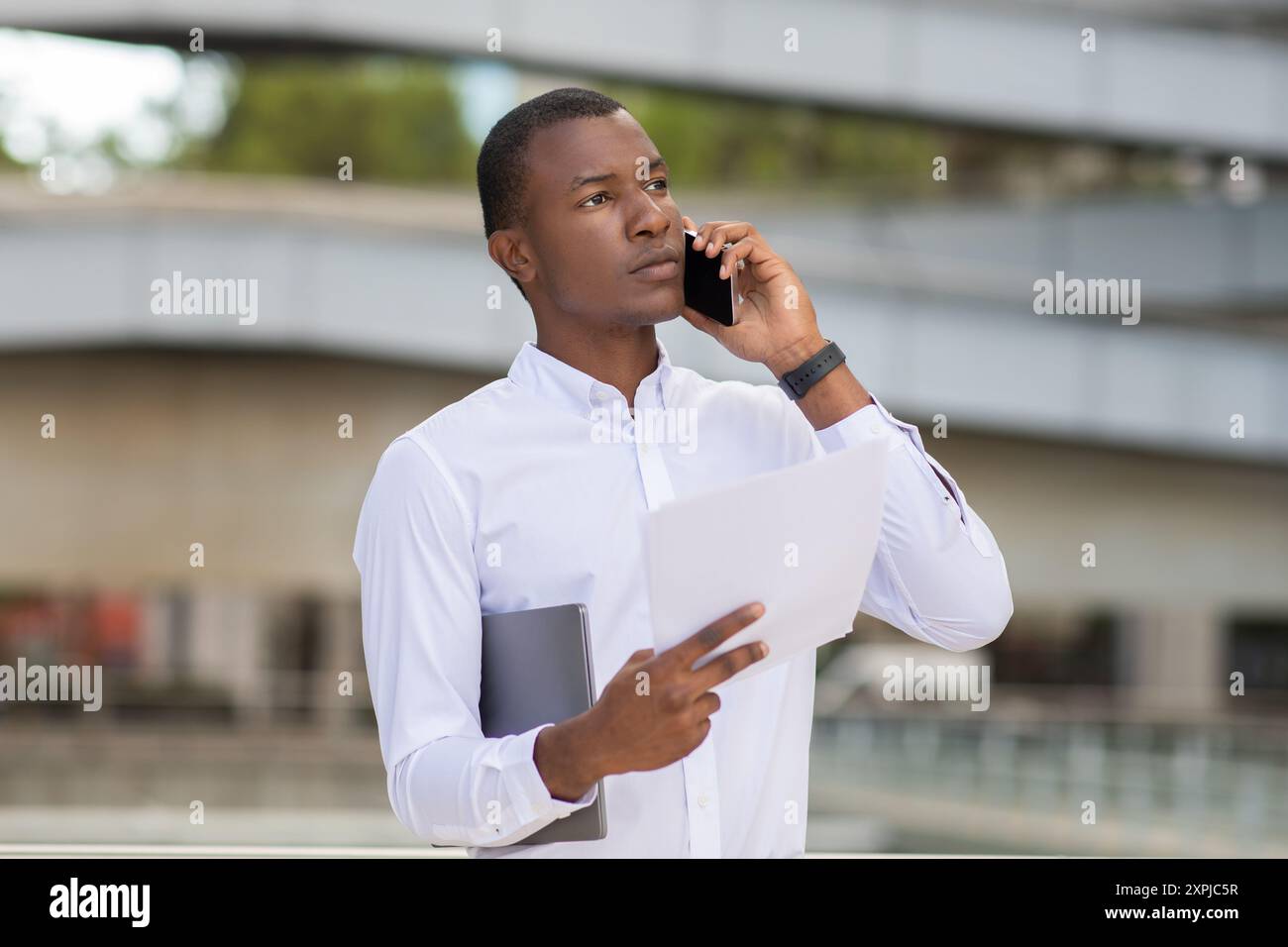 Young Man Engaged in a Phone Conversation While Holding Documents Stock Photo