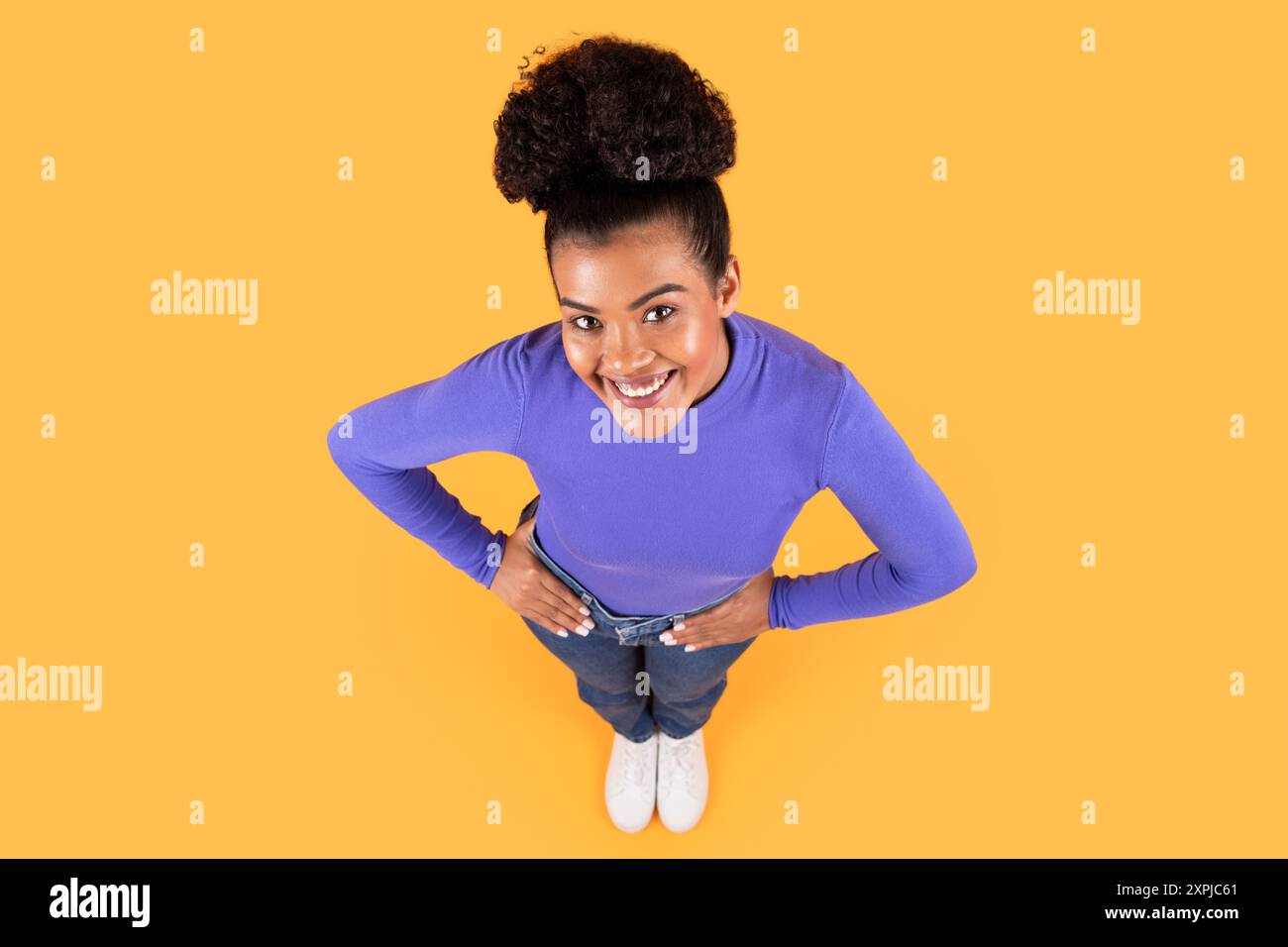Young Woman Smiling Joyfully While Posing On Yellow Stock Photo