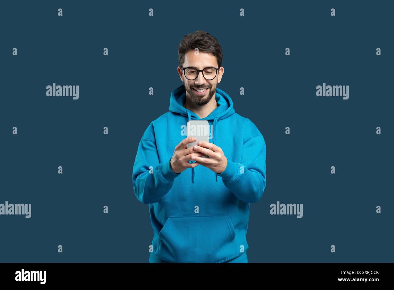 Young Man in Blue Hoodie Smiling While Using Smartphone Stock Photo