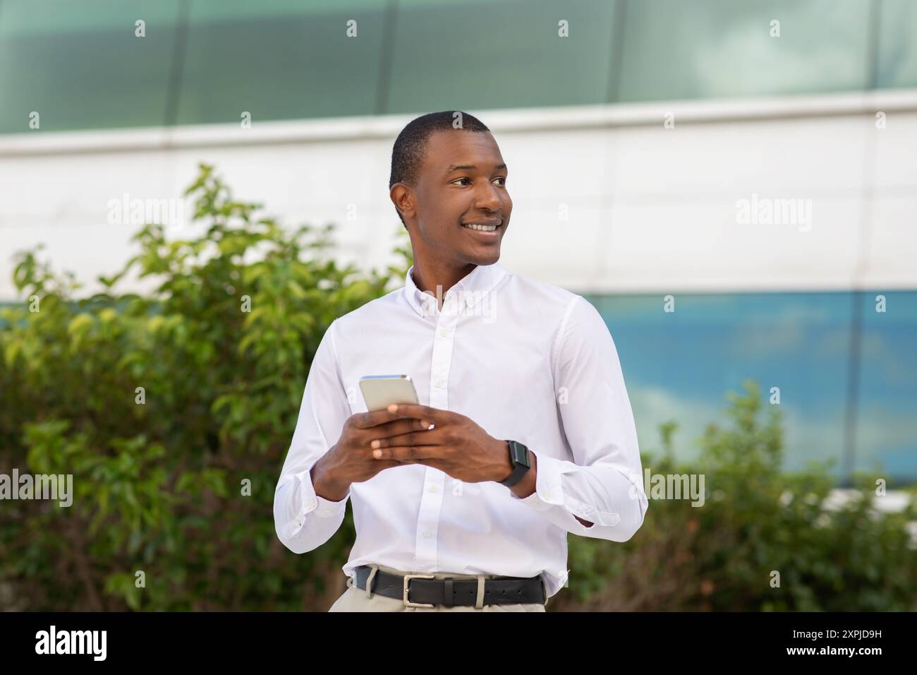 Young Man Smiling While Using Smartphone Near Modern Building Stock Photo