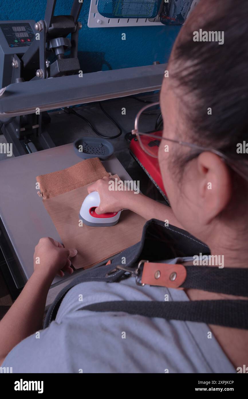 Young working woman in her workshop makes the sublimation process with a label plate, printing and graphic design concept. Stock Photo