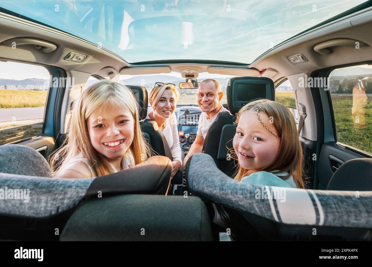 Young couple with daughters portrait sitting in a modern car with a transparent roof. Happy family moments, childhood, fast food eating or auto journe Stock Photo