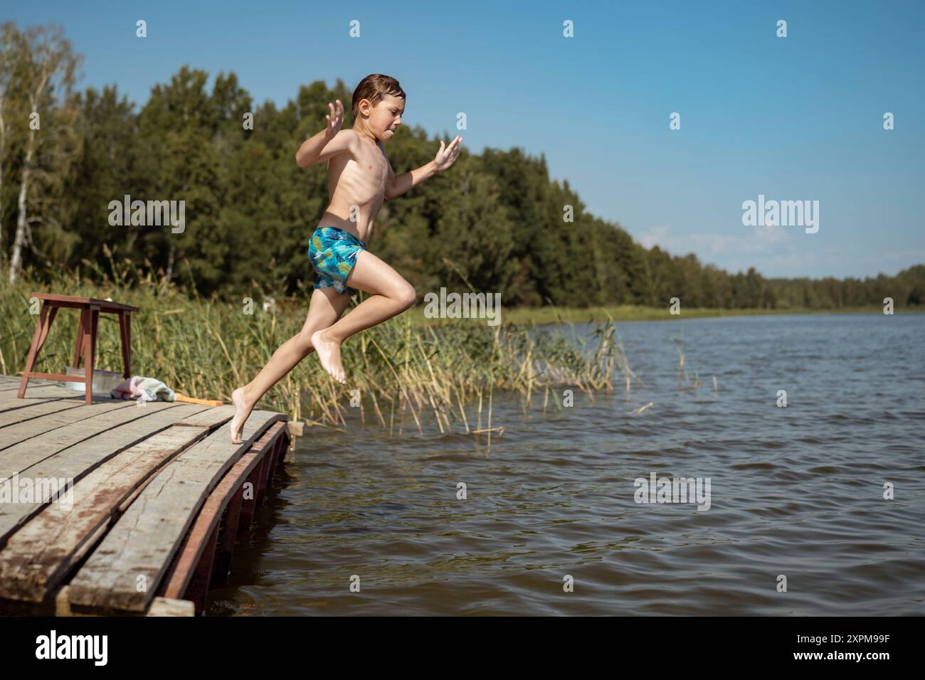 cute caucasian boy jumping from wooden pier diving into lake in ...