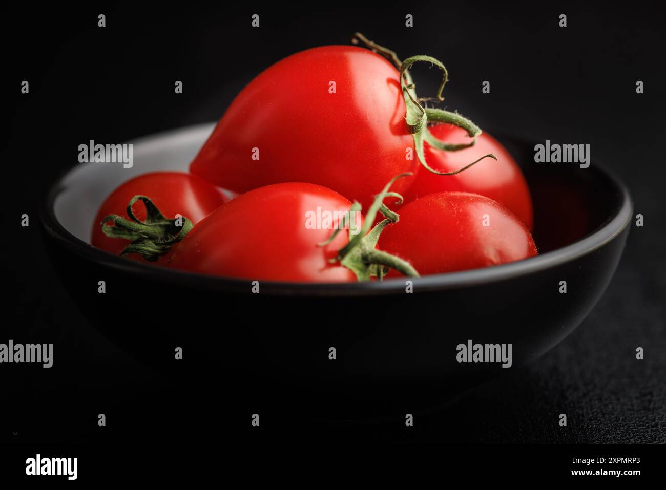 Red cherry tomatoes in bowl on a black table. Stock Photo