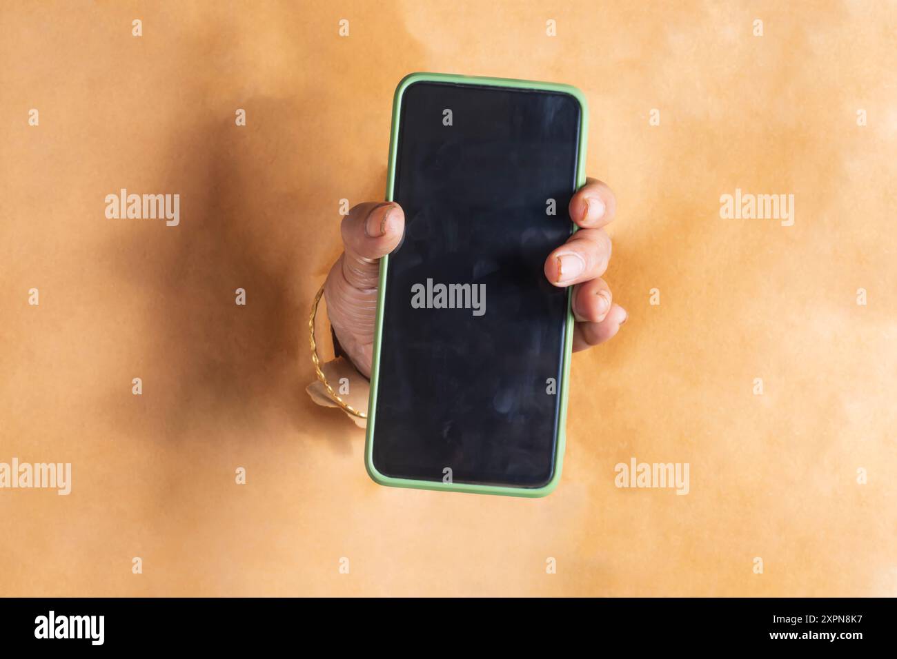 Close-up of woman hand holding mobile phone through torn paper 