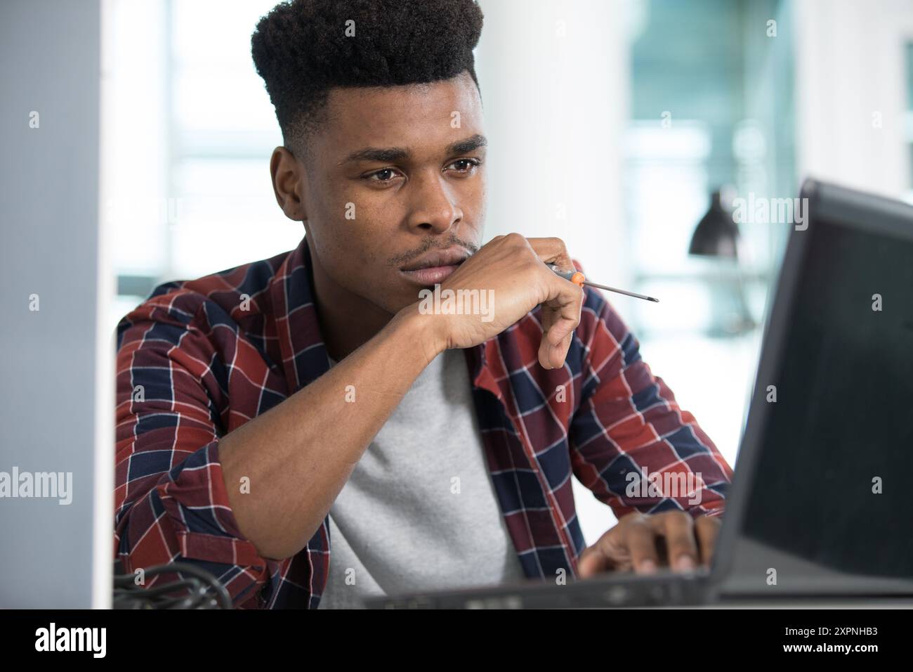 young man works on his laptop and holding a screwdriver Stock Photo