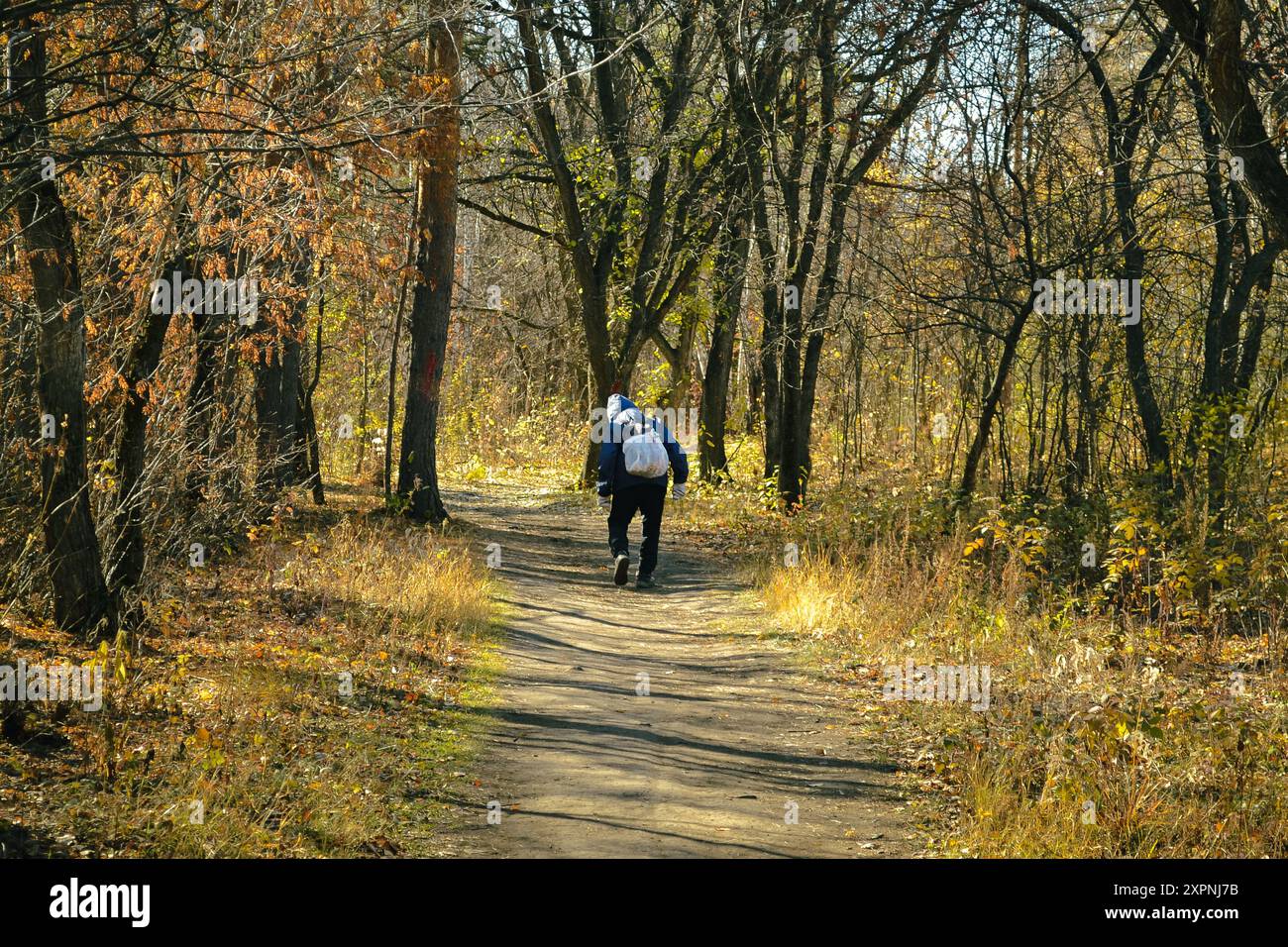 An elderly man with a white bag on his back walks along a path in the ...