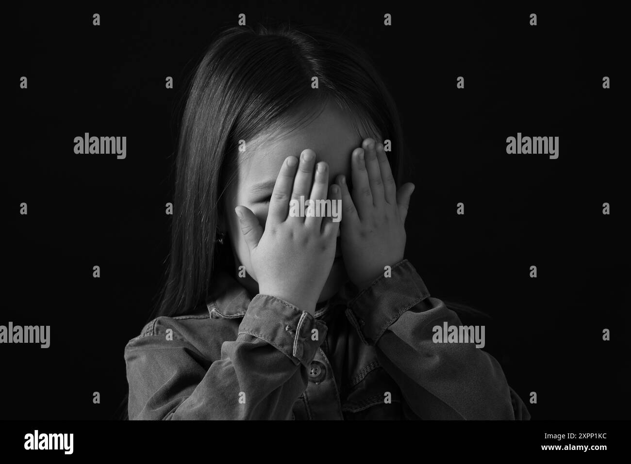 Girl covering face with hands on dark background, closeup. Black and white effect Stock Photo