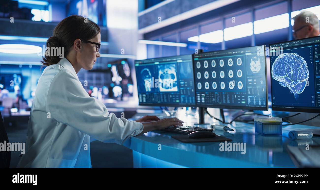 Caucasian Female Neuroscientist Using Desktop Computer To Analyze CT Scans Of Human Brain In Busy Research Center Laboratory. Proffesional Doctor Finding Solutions for Brain Damage, Cancer Treatment. Stock Photo