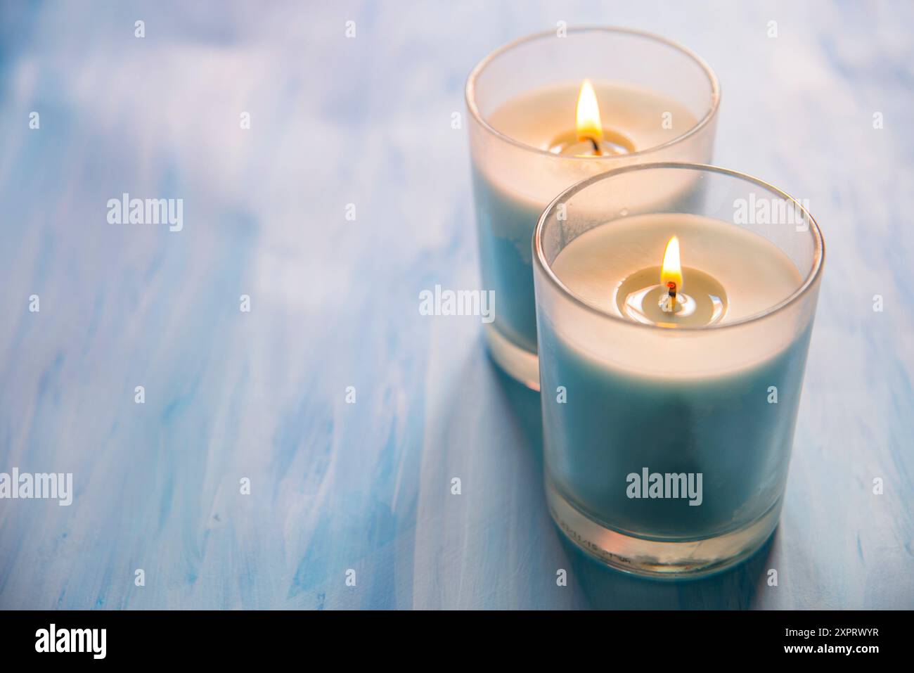 Two lit up candles on blue surface. Stock Photo