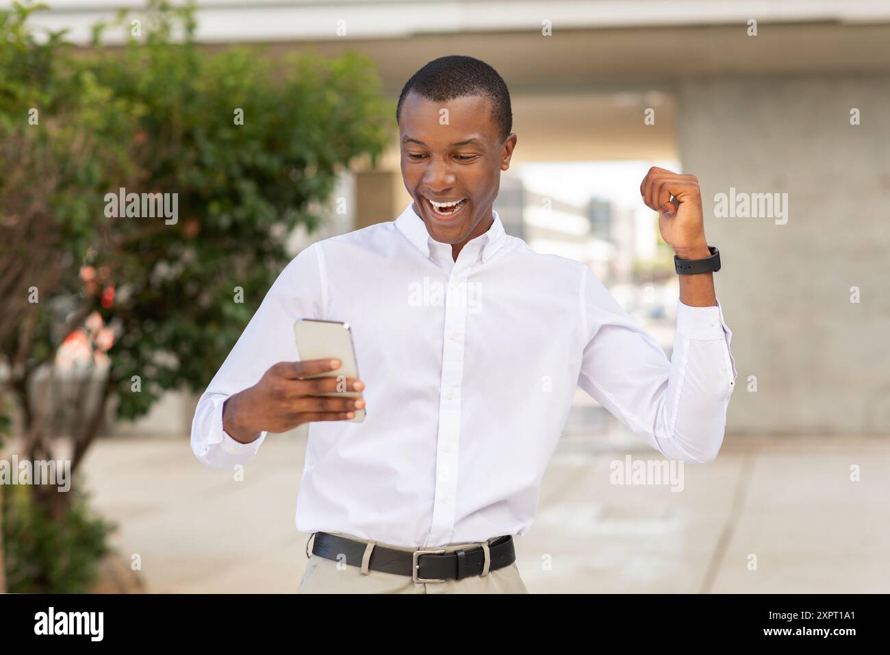 Excited Young Man Celebrating While Checking His Smartphone Outdoors Stock Photo