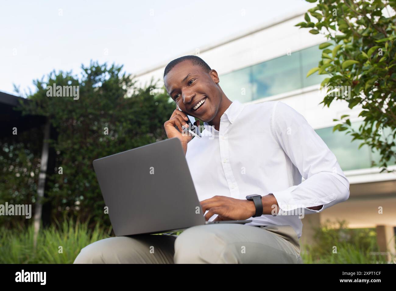 Young Man Working Remotely on Laptop While Talking on Phone Stock Photo