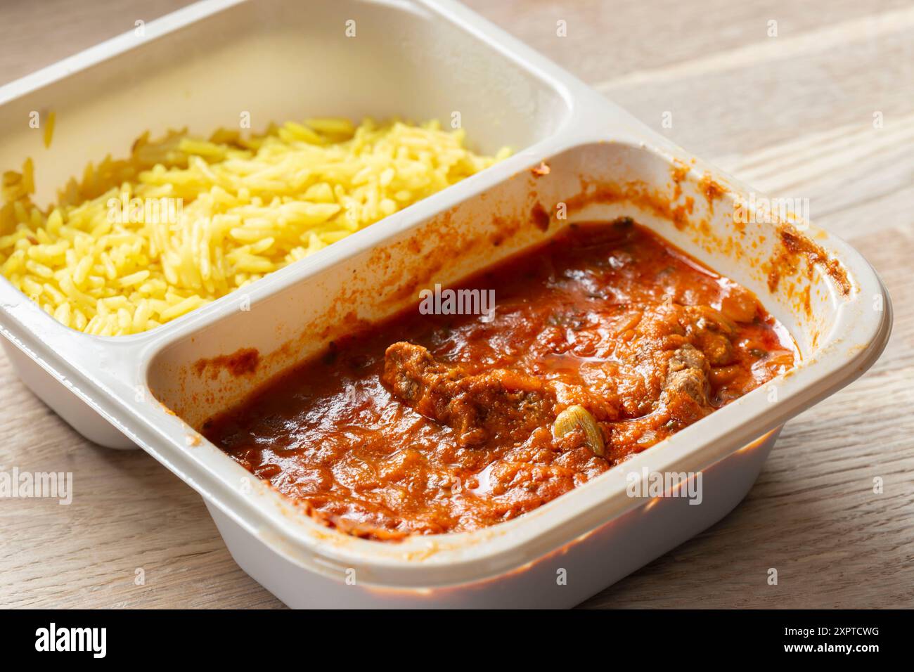 Lamb Rogan Josh Indian curry with pilau rice ready meal in microwave proof packaging. On wood board background Stock Photo