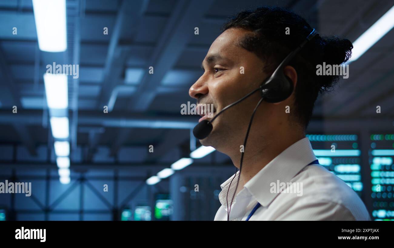 System administrator in data center managing and maintaining databases, ensuring data integrity, security and availability. Indian man updating server farm supercomputers systems, camera B Stock Photo